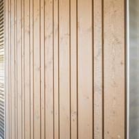 Nahaufnahme einer Fassade in Holzoptik. An den Seiten sind metallene Jalousien zu sehen.