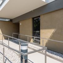 Wohnanlage in der Robert-Stolz-Straße in Linz. Ein modernes, mehrstöckiges Wohngebäude mit hellen Fassaden und zahlreichen Balkonen. Große Fenster sorgen für viel Tageslicht. Vor dem Gebäude stehen Autos auf einer ruhig wirkenden Straße, eingerahmt von gepflegten Grünflächen und Bäumen.