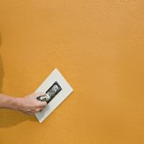 Hand streicht Putz auf Fassade – Schutz und Schönheit in einem Arbeitsschritt