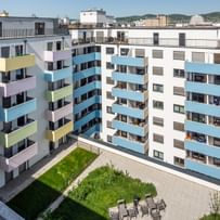 Innenhof von mehrstöckigem Wohnhaus mit weißer Fassade, bunten Balkonen, Wiesenfläche