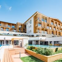 Hotelgebäude mit Holzbalkon und großen Fenstern, das einen Außenpoolbereich umgeben von Grünflächen zeigt. 