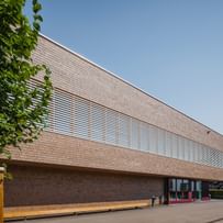Außenansicht eines Gebäudes mit einer hellen Holzfassade. Die Fenster sind mit horizontalen Lamellen ausgestattet