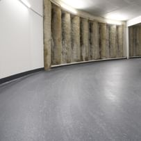 Tiefgarage mit einem gewundenen, grauen Boden und einer Wand, die aus vertikalen, strukturierten Elementen besteht. Die Wände sind weiß und die Beleuchtung ist gleichmäßig.