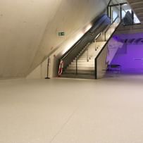 Moderner Ausstellungsraum mit weißen Wänden und Bodenbeschichtung im Schlossmuseum Linz. eine Treppe mit schwarzem Glasgeländer führt hinauf zum Ausgang