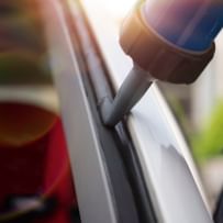 Dichtmittel wird auf die Kante eines Fensters oder einer Tür aufgetragen. Der Fokus liegt auf der Düse des Dichtmittelbehälters.