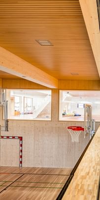 Sporthalle einer Volkshochschule mit einem Fußballtor, einem Basketballkorb und einer Tribüne aus Holz.
