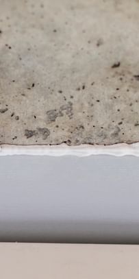 Ein Silikon- oder Dichtmittel wird aus einer Tube auf eine Fuge zwischen einem Betonuntergrund und einer weißen Wandverkleidung aufgetragen.