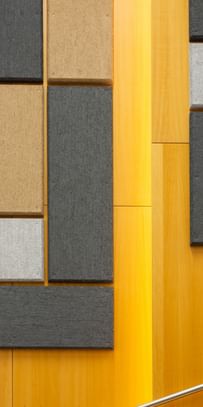 Holzwand mit geometrisch angeordneten Akustikpaneelen in verschiedenen Größen und Farben (Grau, Schwarz, Beige), gestaltet zur Schalloptimierung in der Uni Graz
