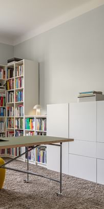 Arbeitszimmer mit Tisch, gelbem Arbeitsstuhl und weißem Bücherregal