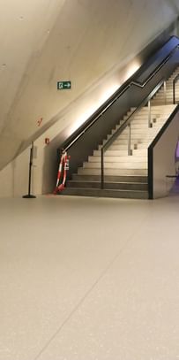 Moderner Ausstellungsraum mit weißen Wänden und Bodenbeschichtung im Schlossmuseum Linz. eine Treppe mit schwarzem Glasgeländer führt hinauf zum Ausgang