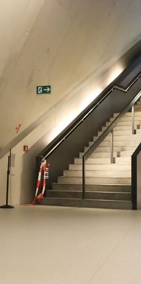 Moderner Ausstellungsraum mit weißen Wänden und Bodenbeschichtung im Schlossmuseum Linz. eine Treppe mit schwarzem Glasgeländer führt hinauf zum Ausgang