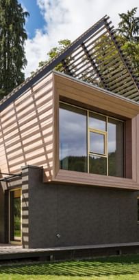 Außenansicht eines modernen Passivhauses mit Holzfassade in natürlichem Grauton, großen Fensterflächen und flach geneigtem Dach, aufgenommen bei Tageslicht im Rahmen der NÖ Landesausstellung in Neubruck, Scheibbs.
