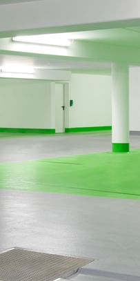 Ein leeres Parkhaus mit grauem Boden und weißen Wänden. Die Säulen sind im unteren Bereich grün gestrichen und der Boden ist in einem Bereich grün markiert.
