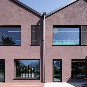 Zweigeschossiges Gebäude mit großen Fenstern. In den oberen Fenstern sind bunte Zeichnungen sichtbar.