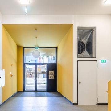 Eingangsbereich Mehrparteienwohnung mit Treppe, gelber Stiege, weißen Wänden Eingangstüre