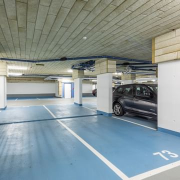 Tiefgarage mit weißen Säulen, blauen Parkflächen und Autos