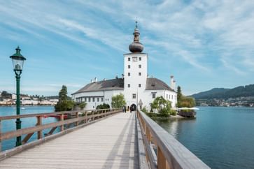 Brücke, umgeben von Wasser, die zum Schloss Orth in weißer Fassade führt