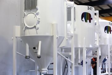 Mehrere große, weiße Silos mit Caparol-Logo und Nummerierung stehen nebeneinander in einer Industriehalle. Eine Person in Warnweste arbeitet im Hintergrund an einem der Silos.