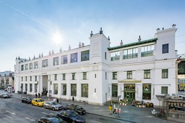 Weißes Gebäude eines U-Bahnhofs mit davor vorbeifahrenden Autos