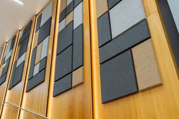Holzwand mit geometrisch angeordneten Akustikpaneelen in verschiedenen Größen und Farben (Grau, Schwarz, Beige), gestaltet zur Schalloptimierung in der Uni Graz