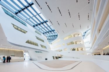 Weitläufiges, lichtdurchflutetes Atrium der Wirtschaftsuniversität Wien mit weißen Wänden, großen Fensterflächen und moderner Architektur.