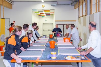Handwerker:innen rund um einen Tisch, vertieft in praxisnahes Schulungstraining mit Musterplatten