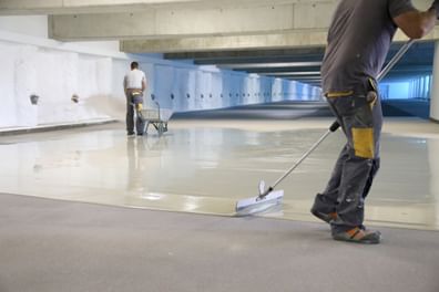 Zwei Fachkräfte tragen Bodenschutz in heller Tiefgarage mit Gefühl für Präzision und Haltbarkeit auf