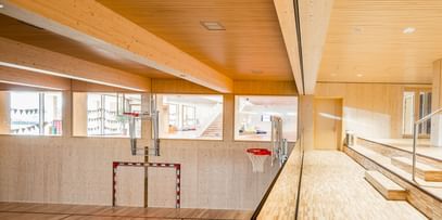 Sporthalle einer Volkshochschule mit einem Fußballtor, einem Basketballkorb und einer Tribüne aus Holz.