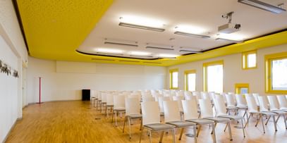 Vortragssaal mit Sesselreihen, Holzboden und gelben Deckenelementen