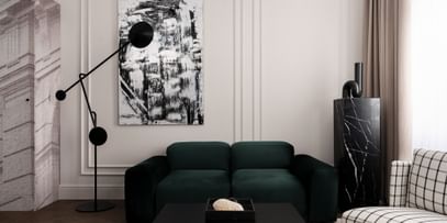 Eleganter Loungebereich einer Executive Suite im „The Amauris“ Wien mit tiefgrünem Samtsofa, großem abstraktem Schwarz-Weiß-Gemälde, skulpturaler schwarzer Stehleuchte, schwarzem Marmorsockel und bodenlangen beigefarbenen Vorhängen.