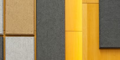 Holzwand mit geometrisch angeordneten Akustikpaneelen in verschiedenen Größen und Farben (Grau, Schwarz, Beige), gestaltet zur Schalloptimierung in der Uni Graz