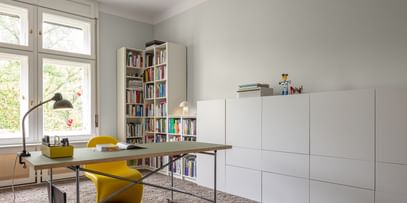 Arbeitszimmer mit Tisch, gelbem Arbeitsstuhl und weißem Bücherregal