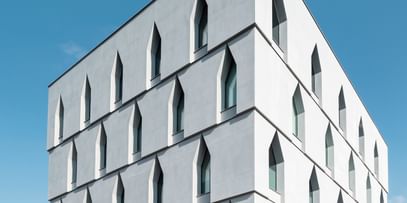 Außenansicht eines mehrstöckigen weißen Gebäudes mit großen, schmalen Fenstern, die in einer einzigartigen, spitz zulaufenden Form angeordnet sind