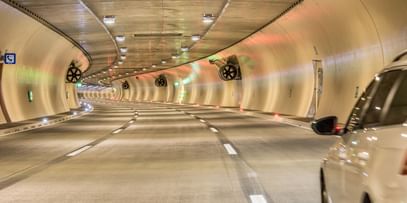 EinTunnel mit sanft geschwungenen Wänden, beleuchtet von bunten Lichtern und auf der rechten Seite ist ein Auto zu sehen, das in den Tunnel einfährt. 
