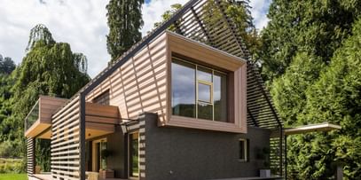 Außenansicht eines modernen Passivhauses mit Holzfassade in natürlichem Grauton, großen Fensterflächen und flach geneigtem Dach, aufgenommen bei Tageslicht im Rahmen der NÖ Landesausstellung in Neubruck, Scheibbs.