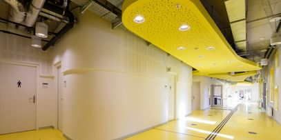 Gang mit gelbem Boden, weiße Wände und industrieller Belüftung an der Decke