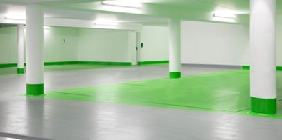 Ein leeres Parkhaus mit grauem Boden und weißen Wänden. Die Säulen sind im unteren Bereich grün gestrichen und der Boden ist in einem Bereich grün markiert.