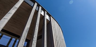 Holzfassade eines Gebäudes von unten. Man blickt auf einen blauen Himmel.