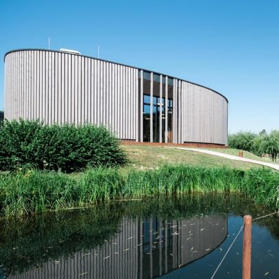 Rundes Holzgebäude spiegelt sich im Teich – Architektur im Einklang mit Natur