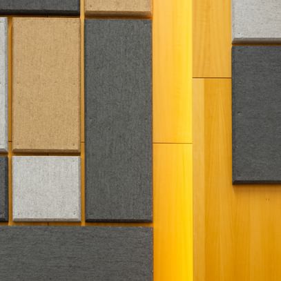 Holzwand mit geometrisch angeordneten Akustikpaneelen in verschiedenen Größen und Farben (Grau, Schwarz, Beige), gestaltet zur Schalloptimierung in der Uni Graz