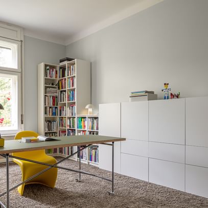 Arbeitszimmer mit Tisch, gelbem Arbeitsstuhl und weißem Bücherregal