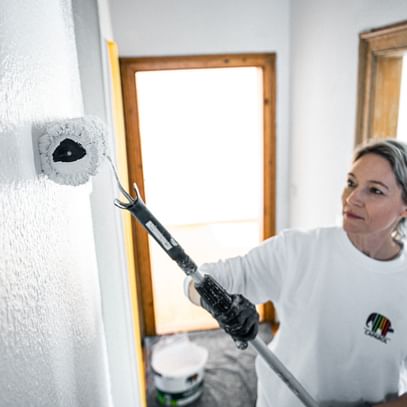 Malerin, die mit einem Farbrolle eine weiße Wand streicht