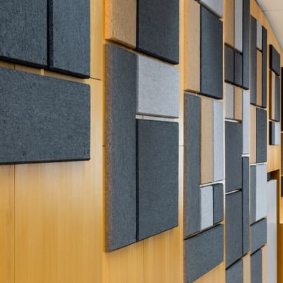 Holzwand mit geometrisch angeordneten Akustikpaneelen in verschiedenen Größen und Farben (Grau, Schwarz, Beige), gestaltet zur Schalloptimierung in der Uni Graz