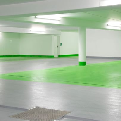 Ein leeres Parkhaus mit grauem Boden und weißen Wänden. Die Säulen sind im unteren Bereich grün gestrichen und der Boden ist in einem Bereich grün markiert.