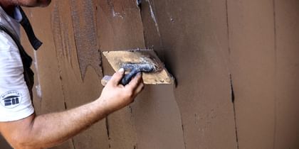 Ein Handwerker trägt braune Putzmasse auf eine Wand auf