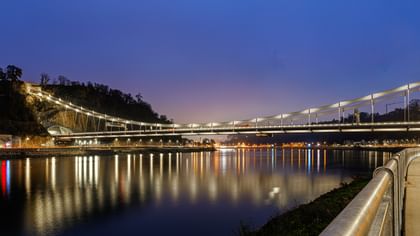 Eine nächtliche Luftaufnahme einer Brücke, die über einen Fluss führt. Die Brücke ist beleuchtet und reflektiert im Wasser.