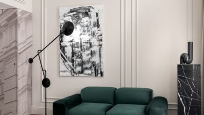 Moderner Sitzbereich im „The Amauris“ Wien mit grünem Samtsofa, hellem Teppich, abstrakter Wandkunst, skulpturaler Stehleuchte, schwarzem Couchtisch, kariertem Sessel und auffälligem, geschwungenen Deckenleuchten-Element.