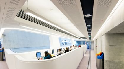 Offener, lichtdurchfluteter Bibliotheksbereich der Wirtschaftsuniversität Wien mit modernen weißen Wänden, großen Fensterflächen und freien Arbeitsplätzen.
