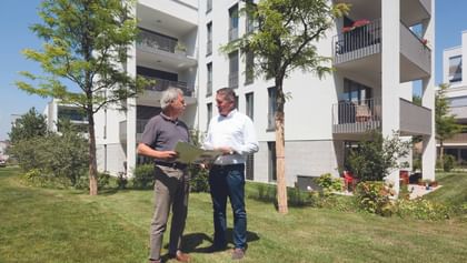 Zwei Männer im Gespräch vor Wohnhaus – Beratung auf Augenhöhe, direkt vor Ort