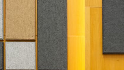 Holzwand mit geometrisch angeordneten Akustikpaneelen in verschiedenen Größen und Farben (Grau, Schwarz, Beige), gestaltet zur Schalloptimierung in der Uni Graz